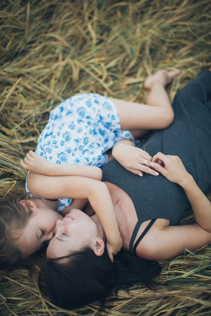 A mother and daughter share a tender moment lying together on a grassy field.